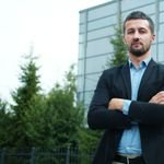 Confident businessman in suit stands with arms crossed outdoors against modern building.