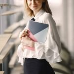 Positive employee in classy formal clothes standing with notebook near window in contemporary office hall
